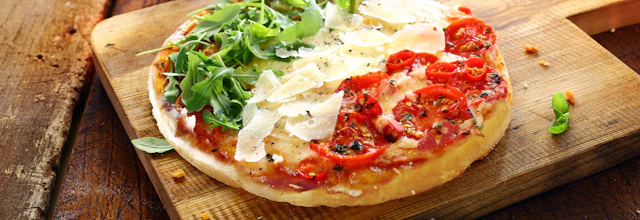 Traditionel italiensk pizza med frisk rucola, cherrytomater og parmesanost på rustikt træbræt
