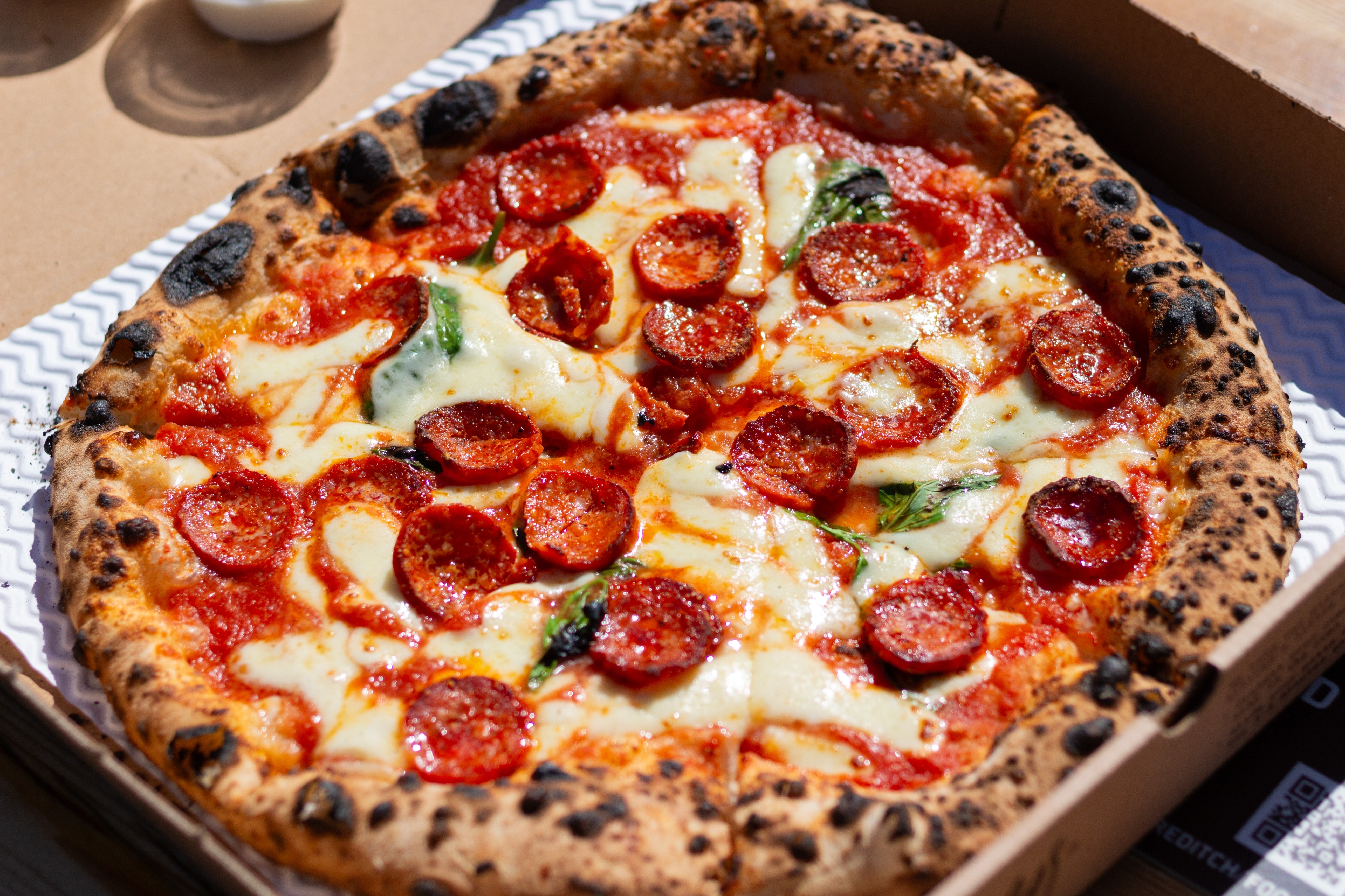 Autentisk napolitansk pizza med pepperoni, mozzarella og basilikum serveret i italiensk restaurant