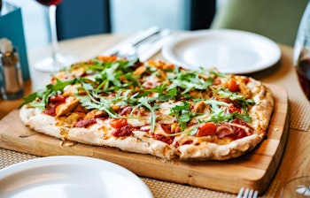 Autentisk italiensk pizza med frisk mozzarella, rucola og tomatsauce serveret med et glas rødvin i en hyggelig restaurant i Italien