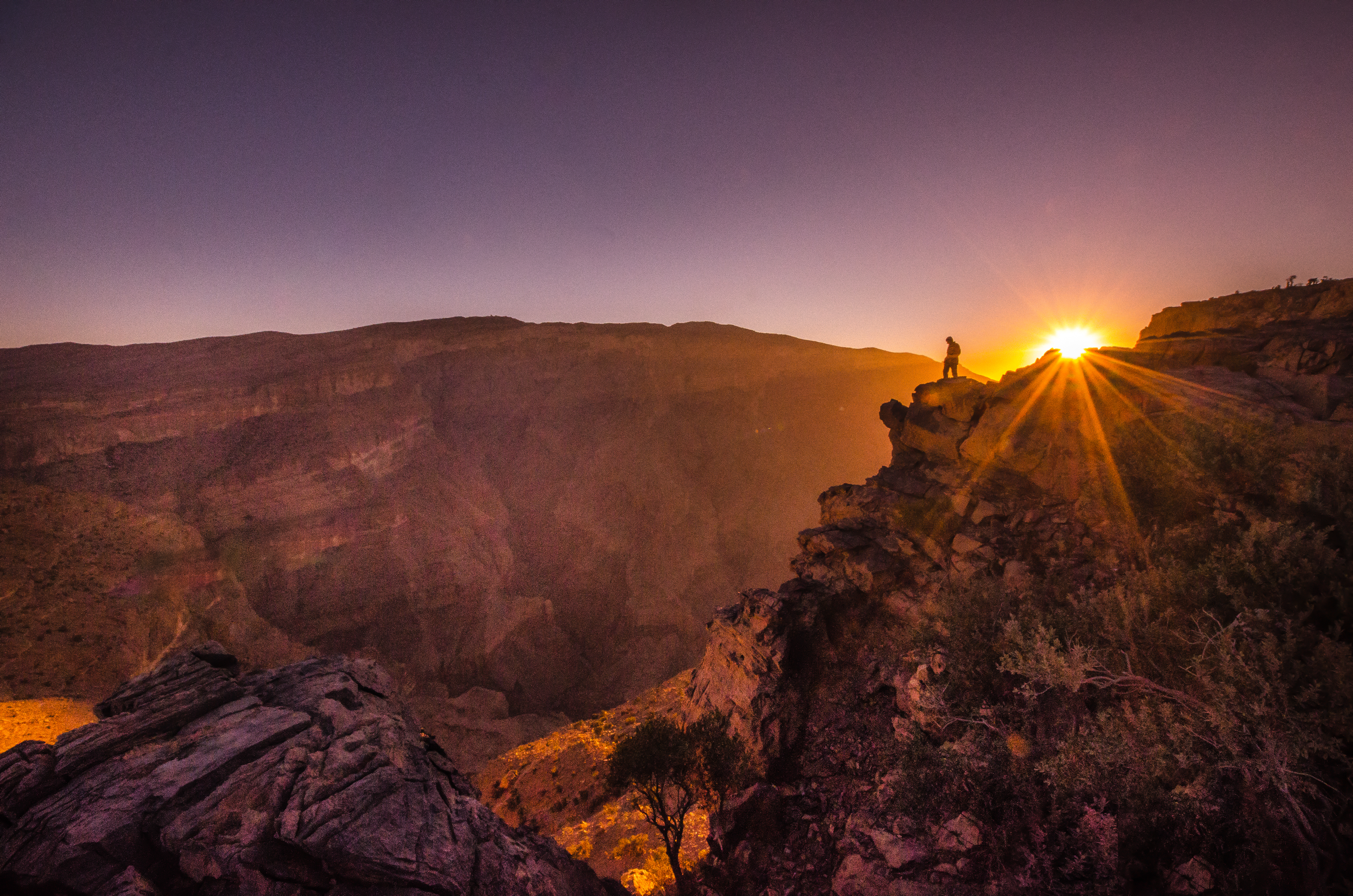 Spektakulær solopgang over Jabal Shams i Oman, hvor solens gyldne stråler bryder gennem skyerne og oplyser det dramatiske bjerglandskab i morgenlyset