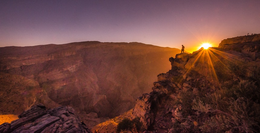 Spektakulær solopgang over Jabal Shams i Oman, hvor solens gyldne stråler bryder gennem skyerne og oplyser det dramatiske bjerglandskab i morgenlyset