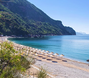 Idyllisk Jaz strand nær Budva i Montenegro med rækker af stråparasoller og krystalklart vand ved Adriaterhavet