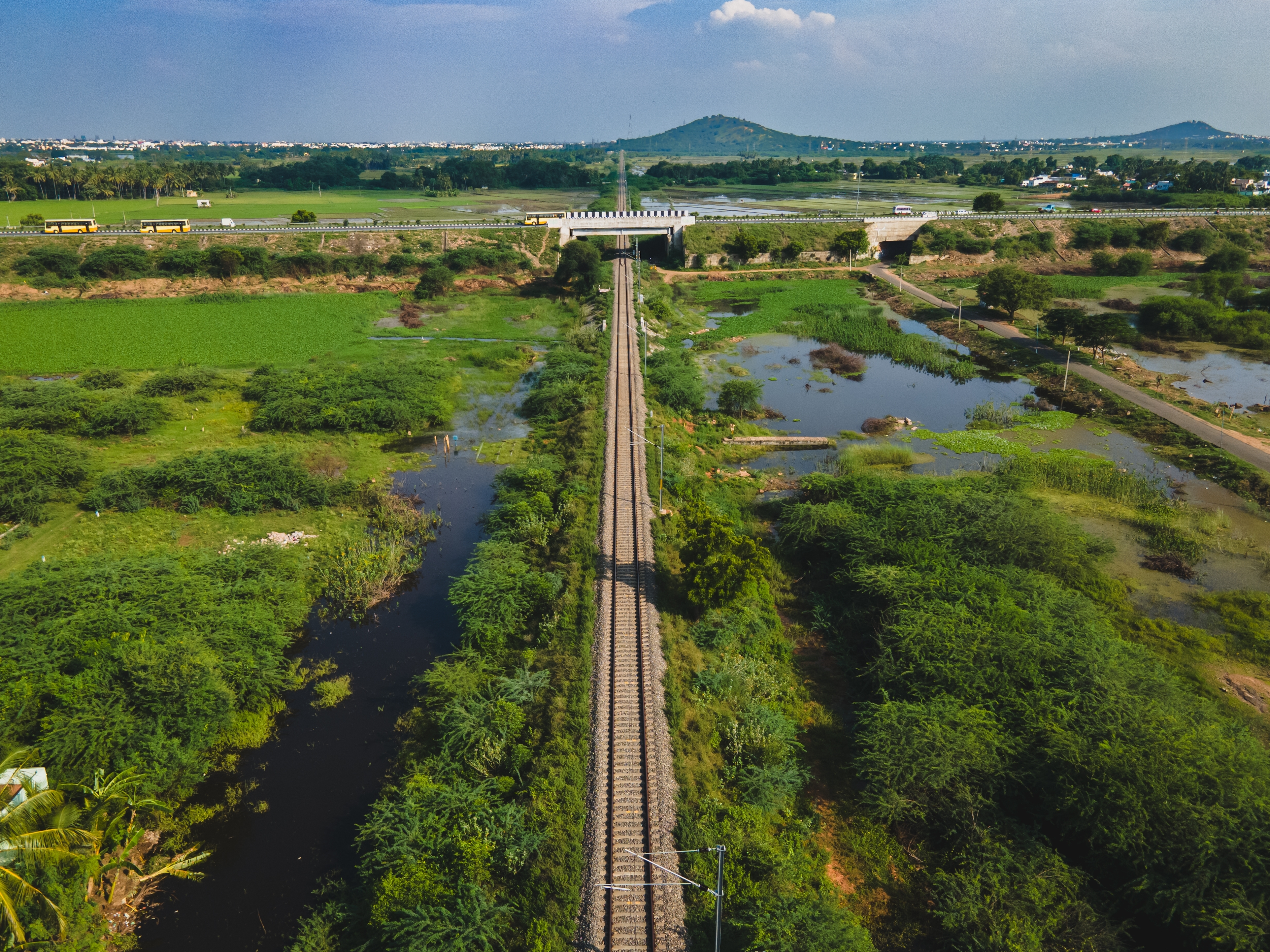 Malerisk jernbanespor gennem Keralas frodige vådområder i Indien med grønne marker og bjerge i horisonten
