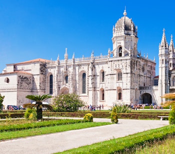 Det historiske Jeronimos Kloster i Lissabon med imponerende Manuelisk arkitektur, dekorativ hvid facade og velholdte haver under blå himmel - UNESCO verdensarv