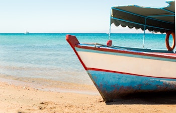 Farverig traditionel træbåd med blå og hvide detaljer på den gyldne sandstrand ved Det Røde Hav i Jordan, perfekt til en afslappende badeferie