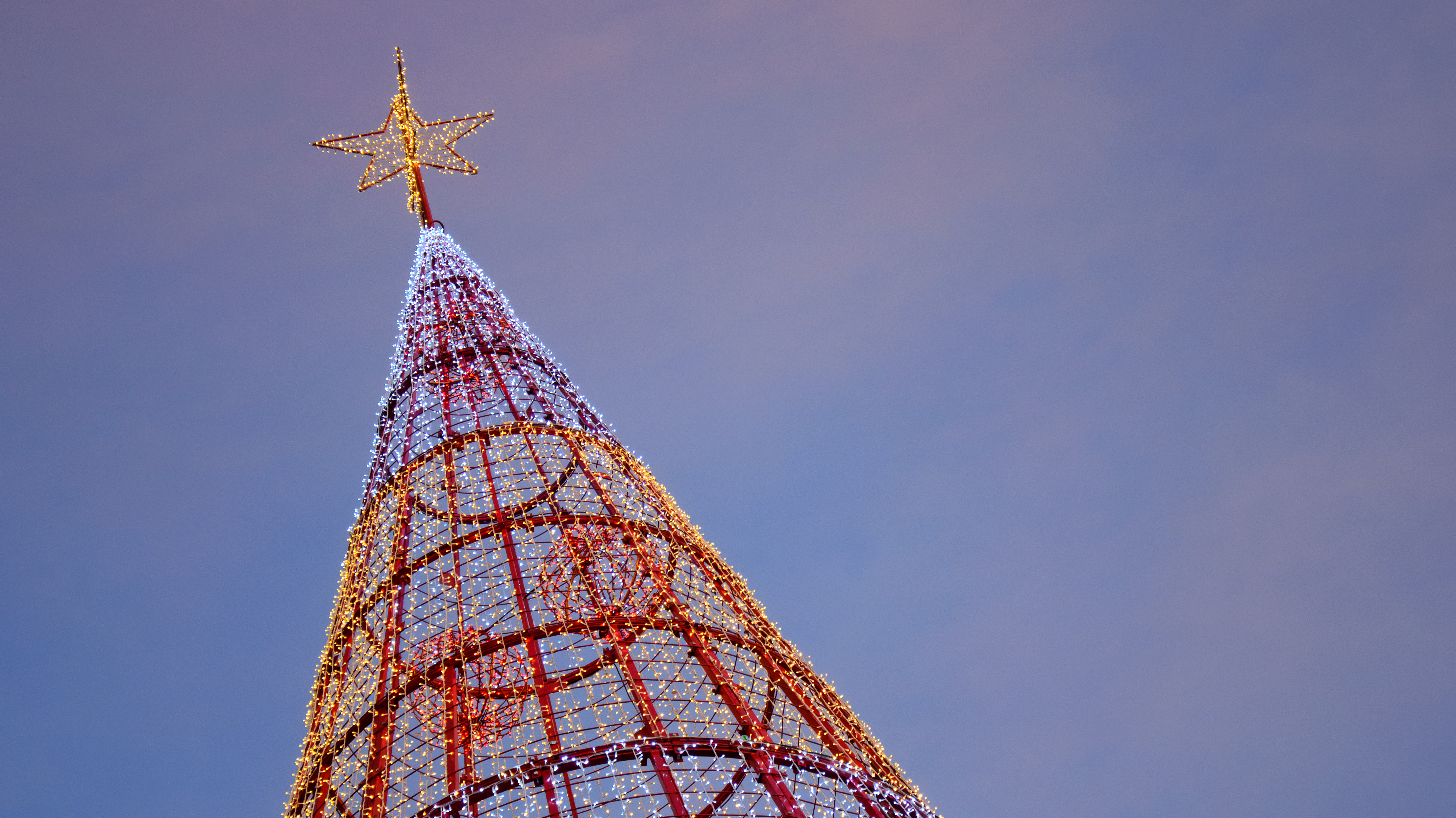 Storslået oplyst juletræ med gyldenstjerne på toppen mod en blå aftenhimmel i Funchal, Madeira