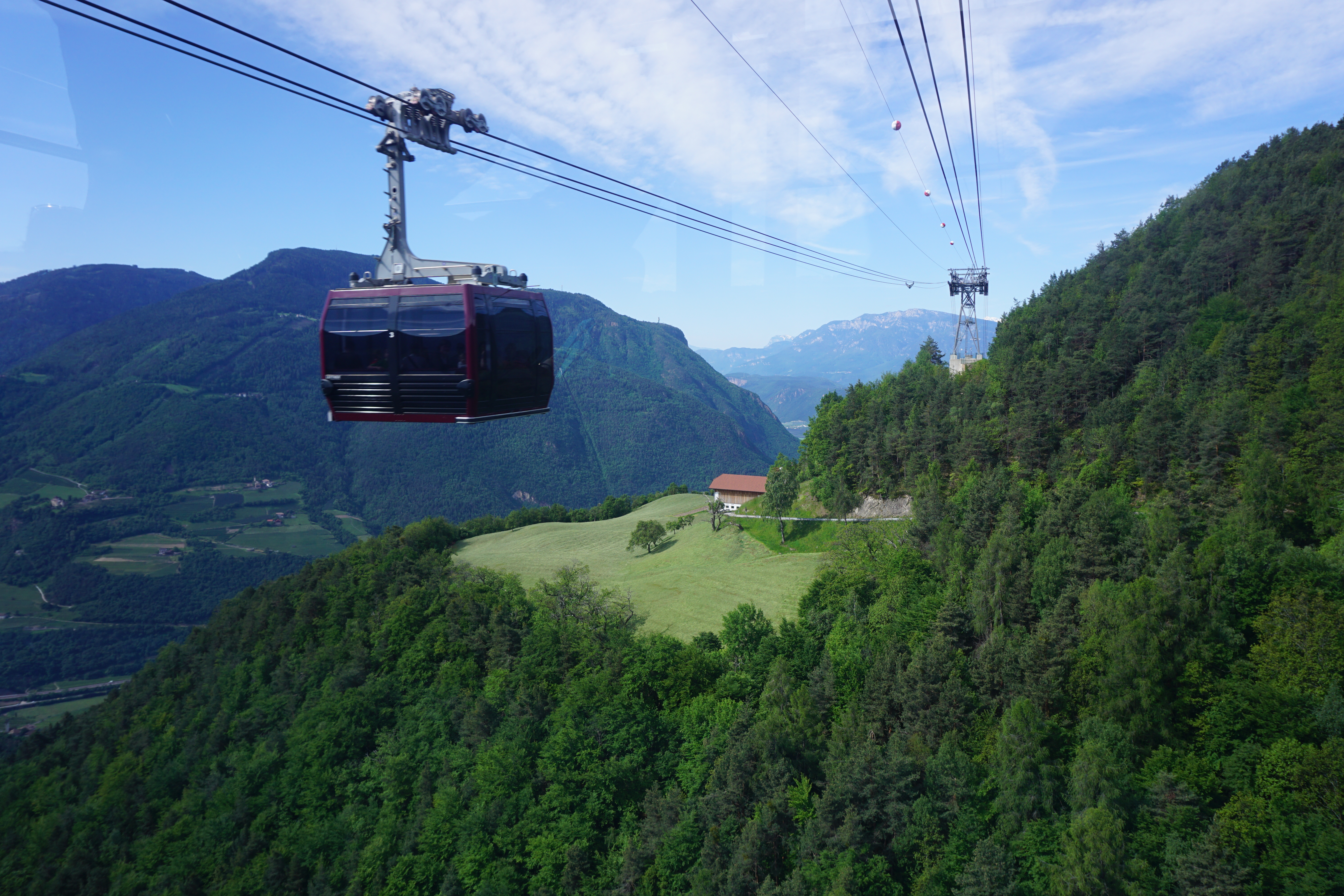 Rød kabelbane svæver over frodig grøn alpeskov med panoramaudsigt over Dolomitterne og dalen ved Bolzano i Sydtyrol, Italien