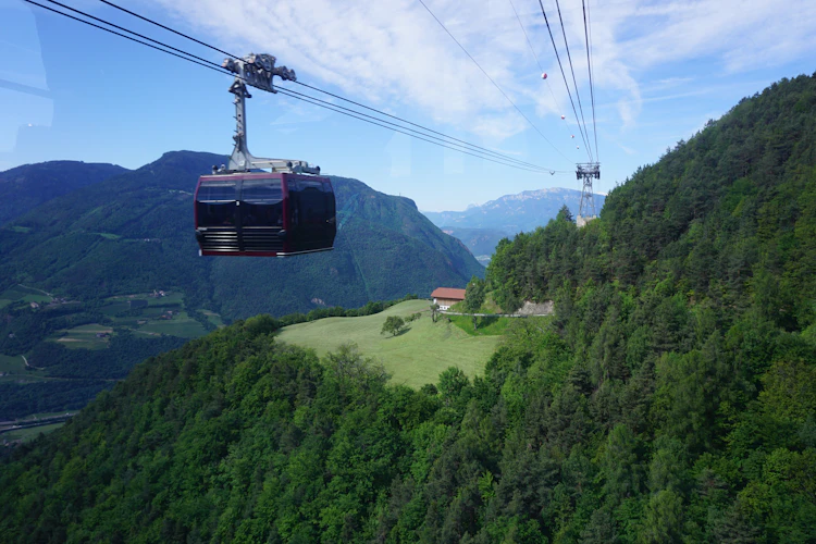 Rød kabelbane svæver over frodig grøn alpeskov med panoramaudsigt over Dolomitterne og dalen ved Bolzano i Sydtyrol, Italien