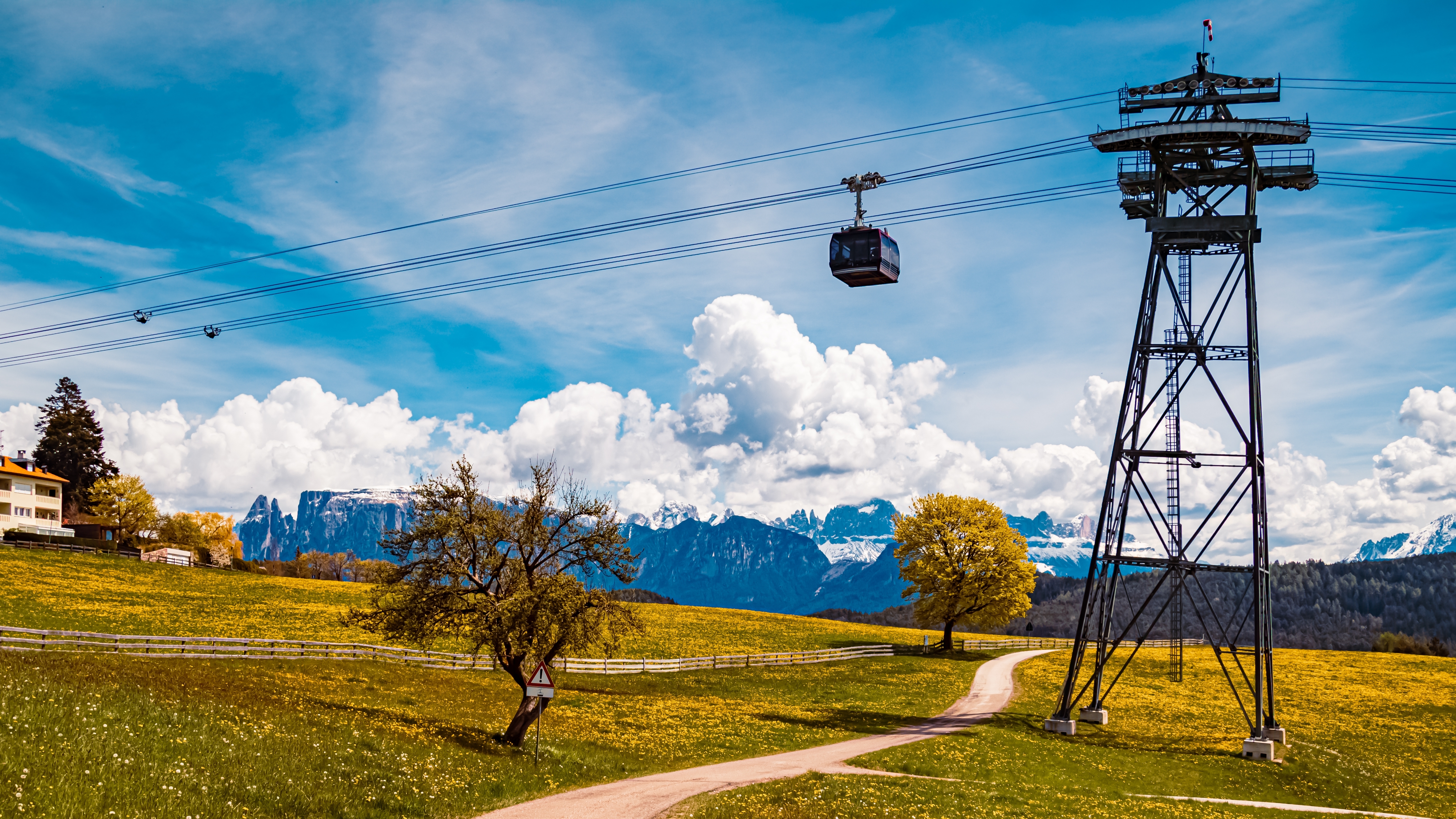 Kabelbane svæver over grønne forårsenge med de imponerende Dolomitter og snedækkede bjergtinder i baggrunden ved Ritten, Sydtyrol, Italien