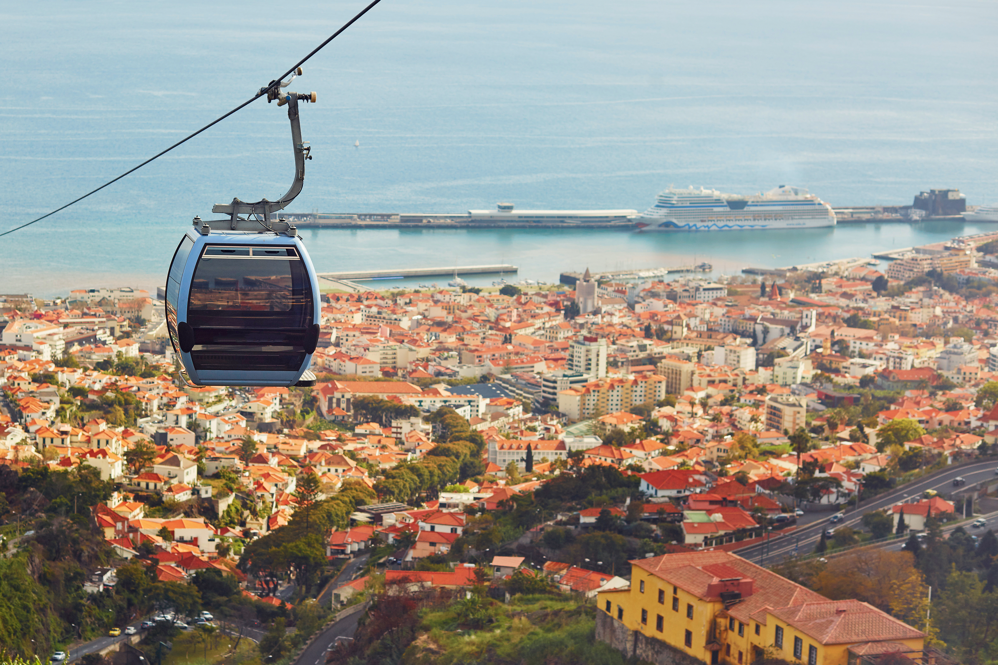 Svævebane over Funchal by med udsigt over røde tegltage, blåt hav og krydstogtskibe i havnen på Madeira, Portugal