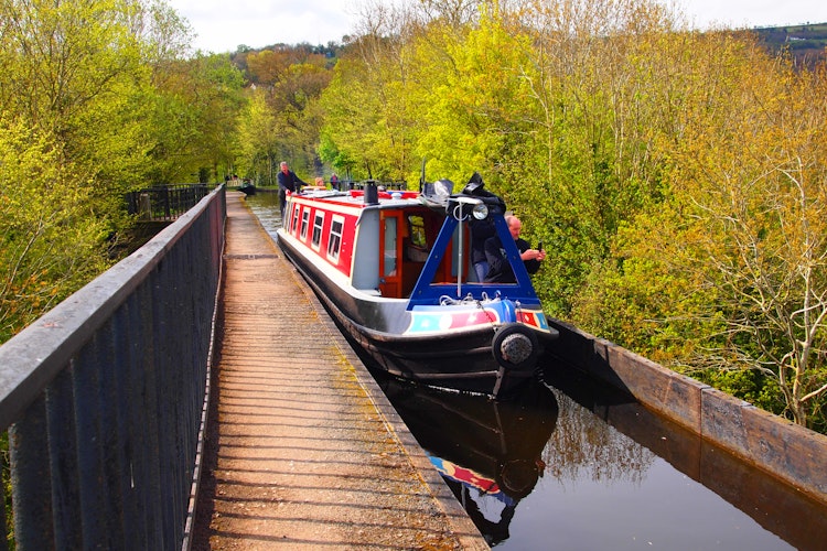 Farverig kanalbaad krydser skoent akvadukt omgivet af frodig groen natur