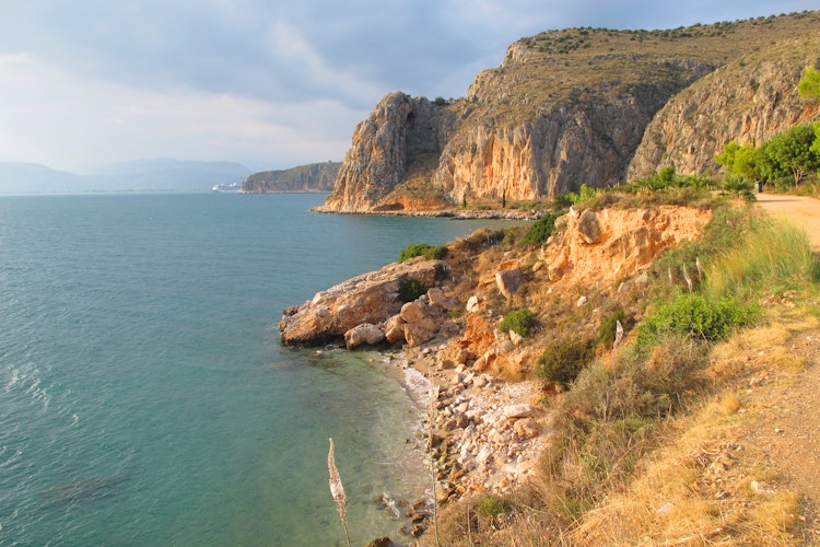 Smuk klippekyst ved Karathonas strand med udsigt til Arvanitia-bakken og Nafplio, Peloponnes, Grækenland