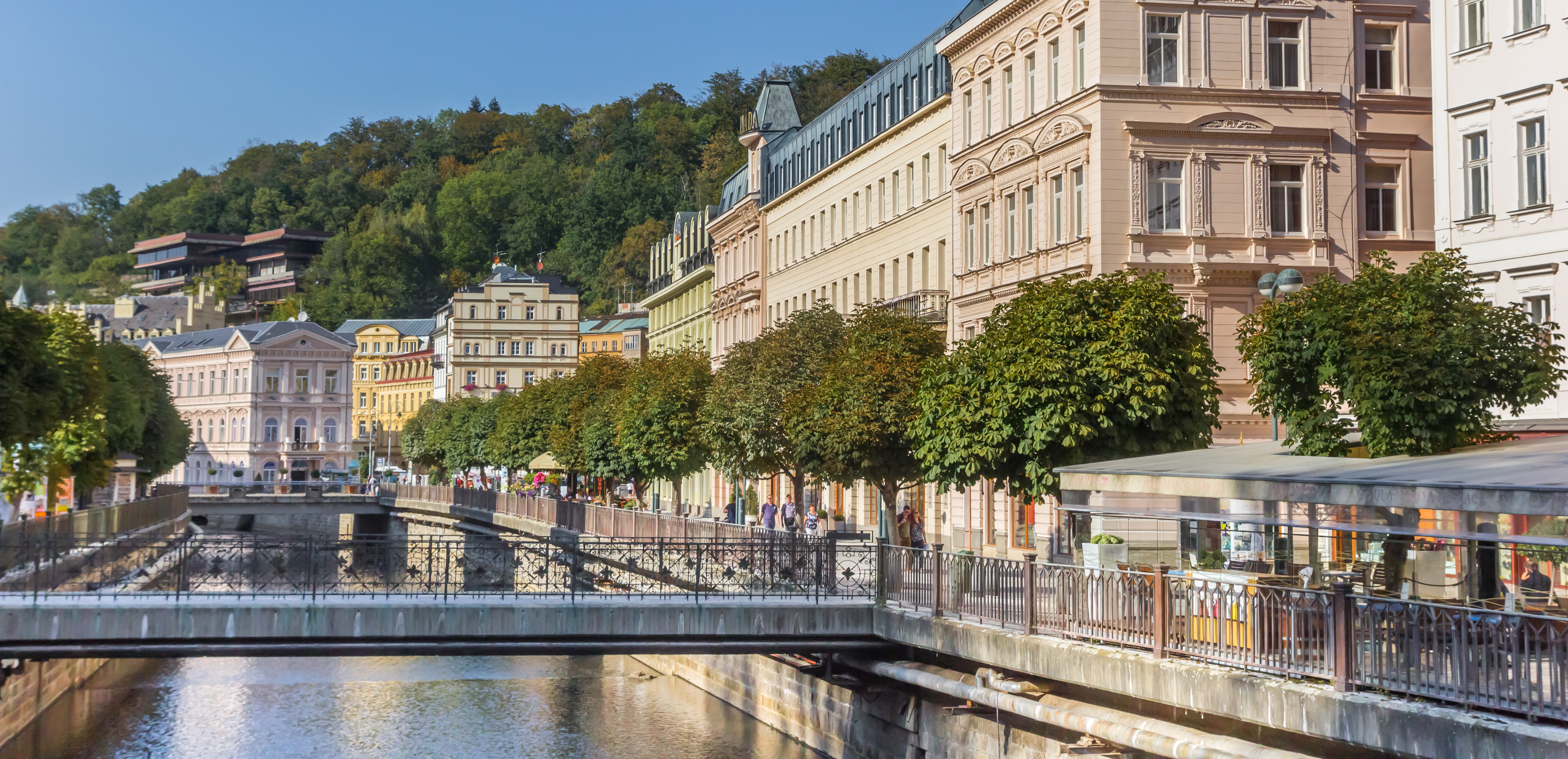 Karlovy Vary flodpromenade med historiske bygninger og grønne træer i tjekkisk kurby
