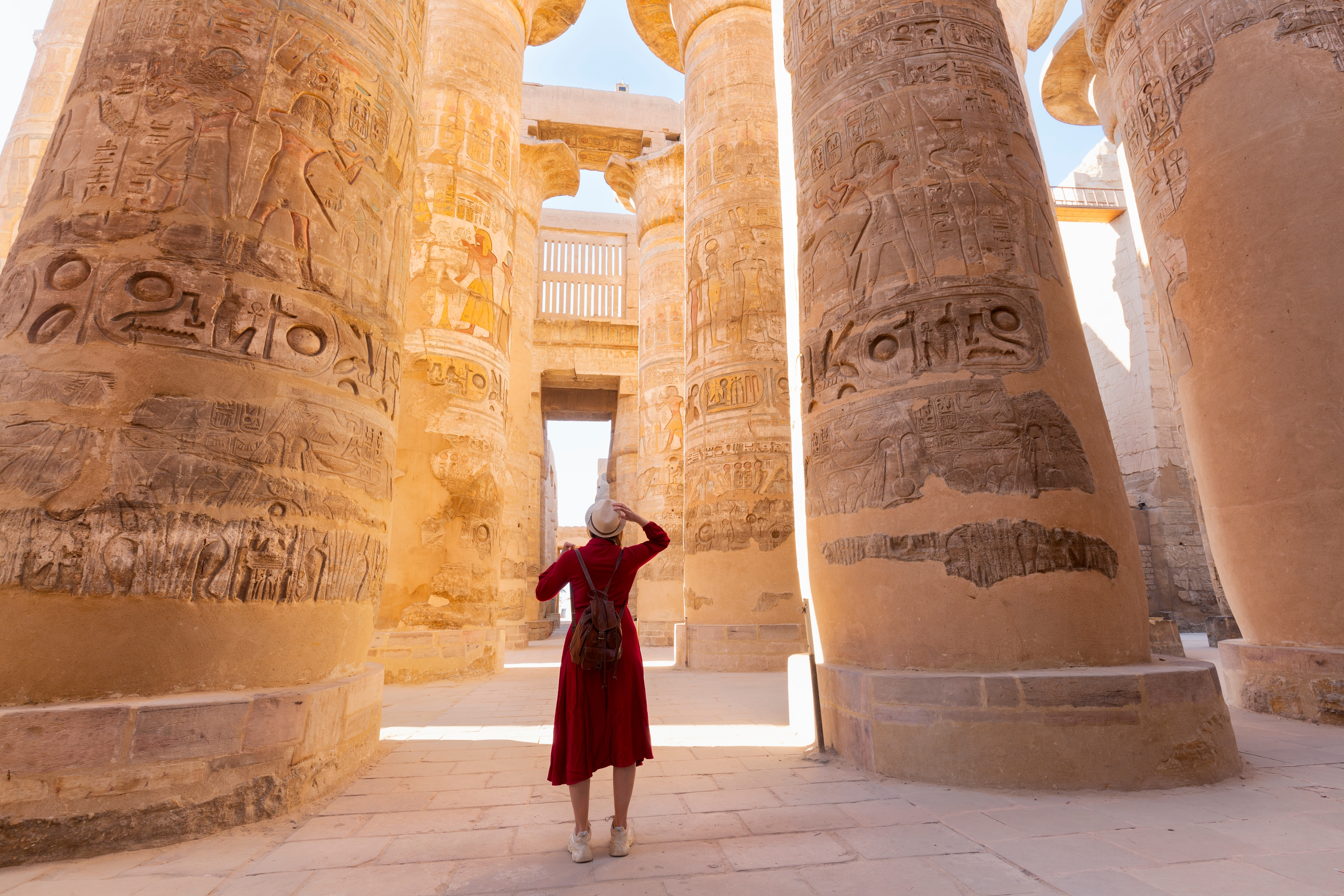 Kvinde i rød kjole udforsker de mægtige søjler med hieroglyffer i Karnak-templet i Luxor, Egypten