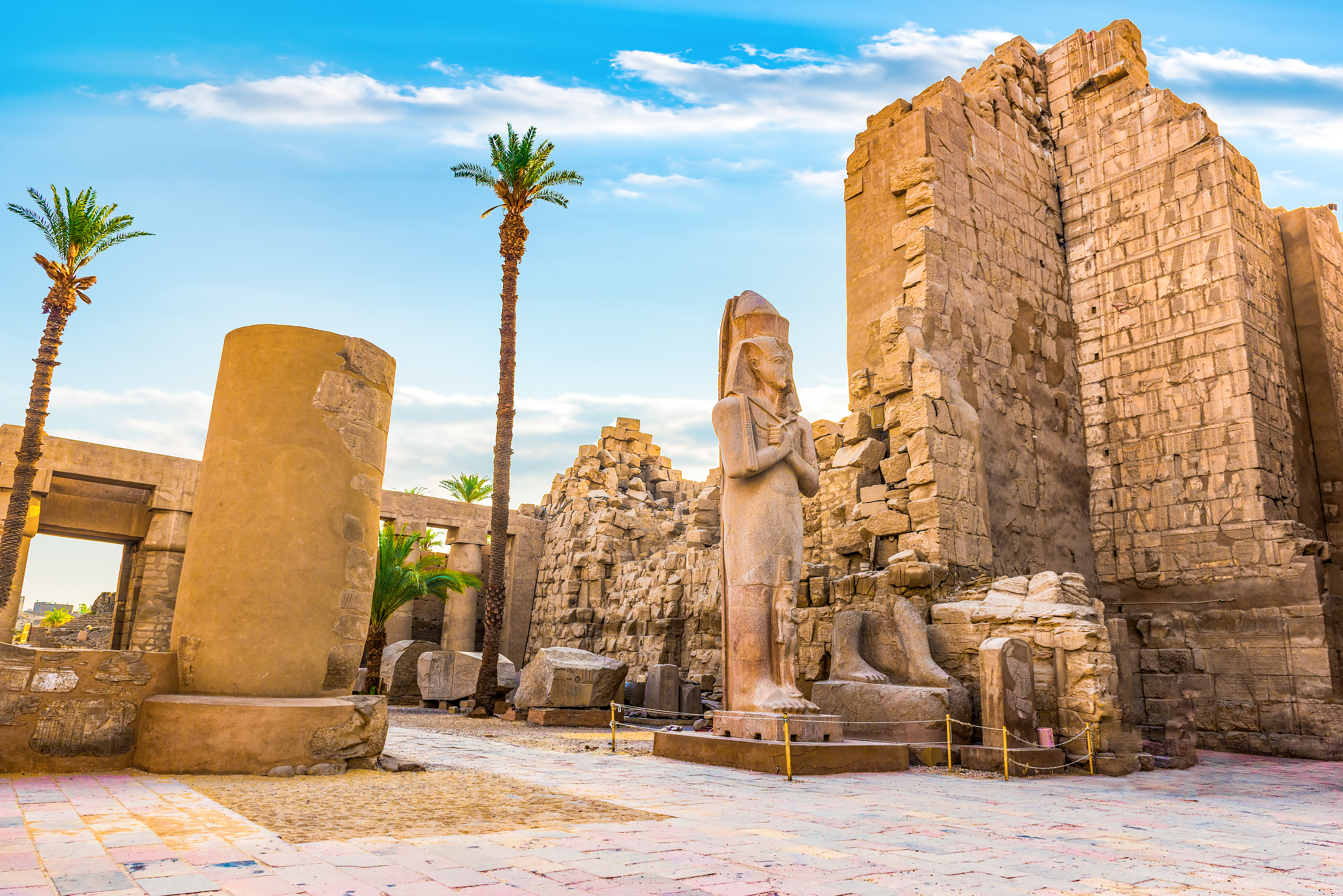 Imponerende ruiner ved Karnak-templet i Luxor, Egypten, med en stor farao-statue og massive stenbyggerier under blå himmel