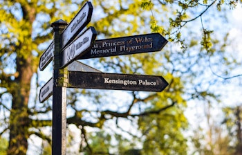 Vejvisningsskilt til Kensington Palace i de smukke Kensington Gardens med frodig grøn natur og historisk atmosfære i London