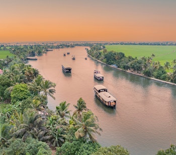 Luftfoto af traditionelle husbaade der sejler gennem Keralas fredelige backwaters i Alleppey, omgivet af frodige kokospalmer og smaragdgrønne kanaler i Indien