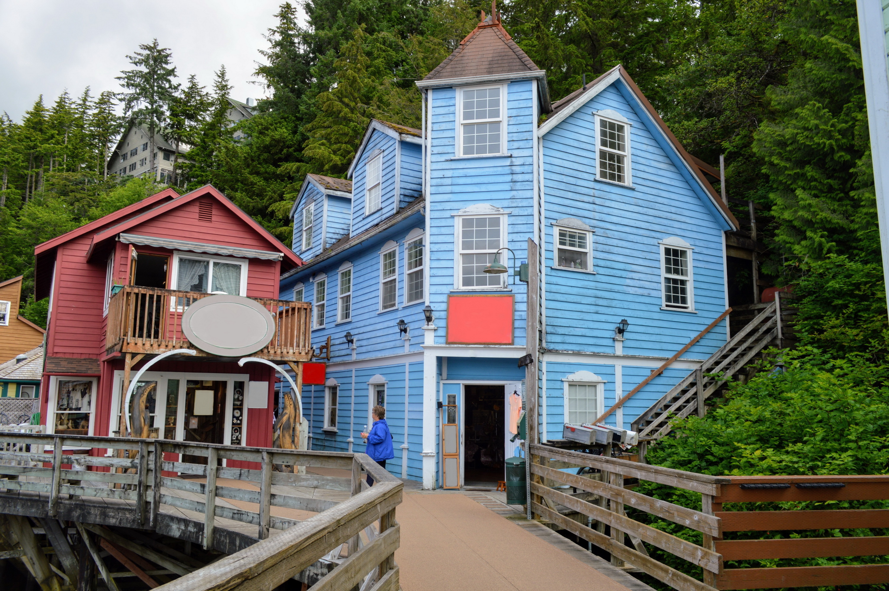 Farverige træhuse på pæle ved Creek Street i Ketchikan, Alaska med gangbro og skov