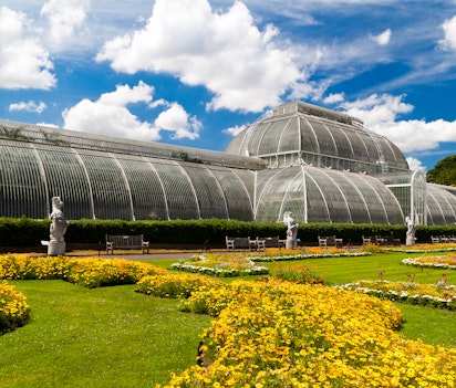 Det historiske victorianske drivhus i Kew Gardens, London, omgivet af velholdte plæner og farverige blomsterbede under en klar blå himmel