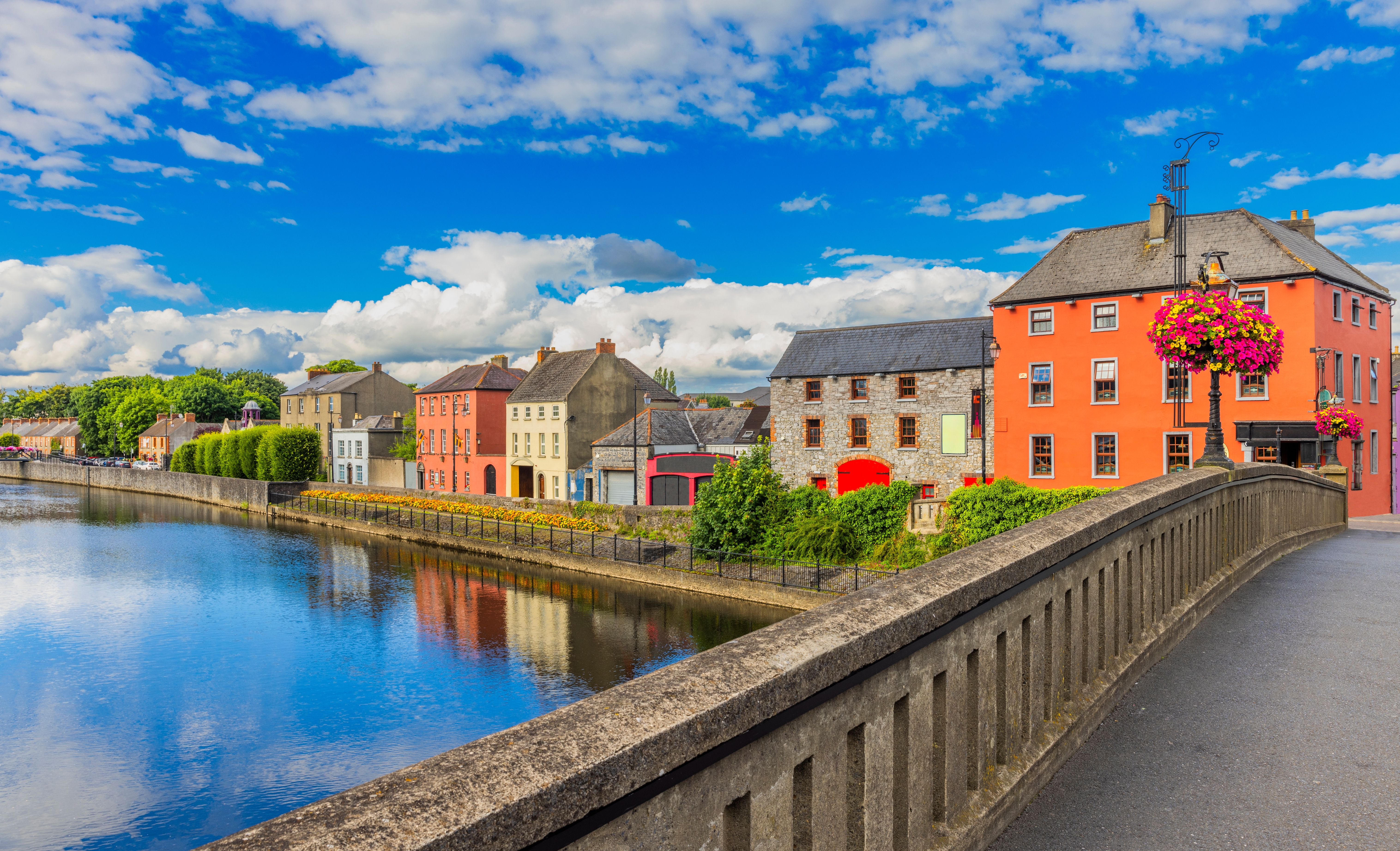 Farverige bygninger langs floden Nore i Kilkenny, Irland, med smukt vejr og blomsterdekorationer på en solrig sommerdag