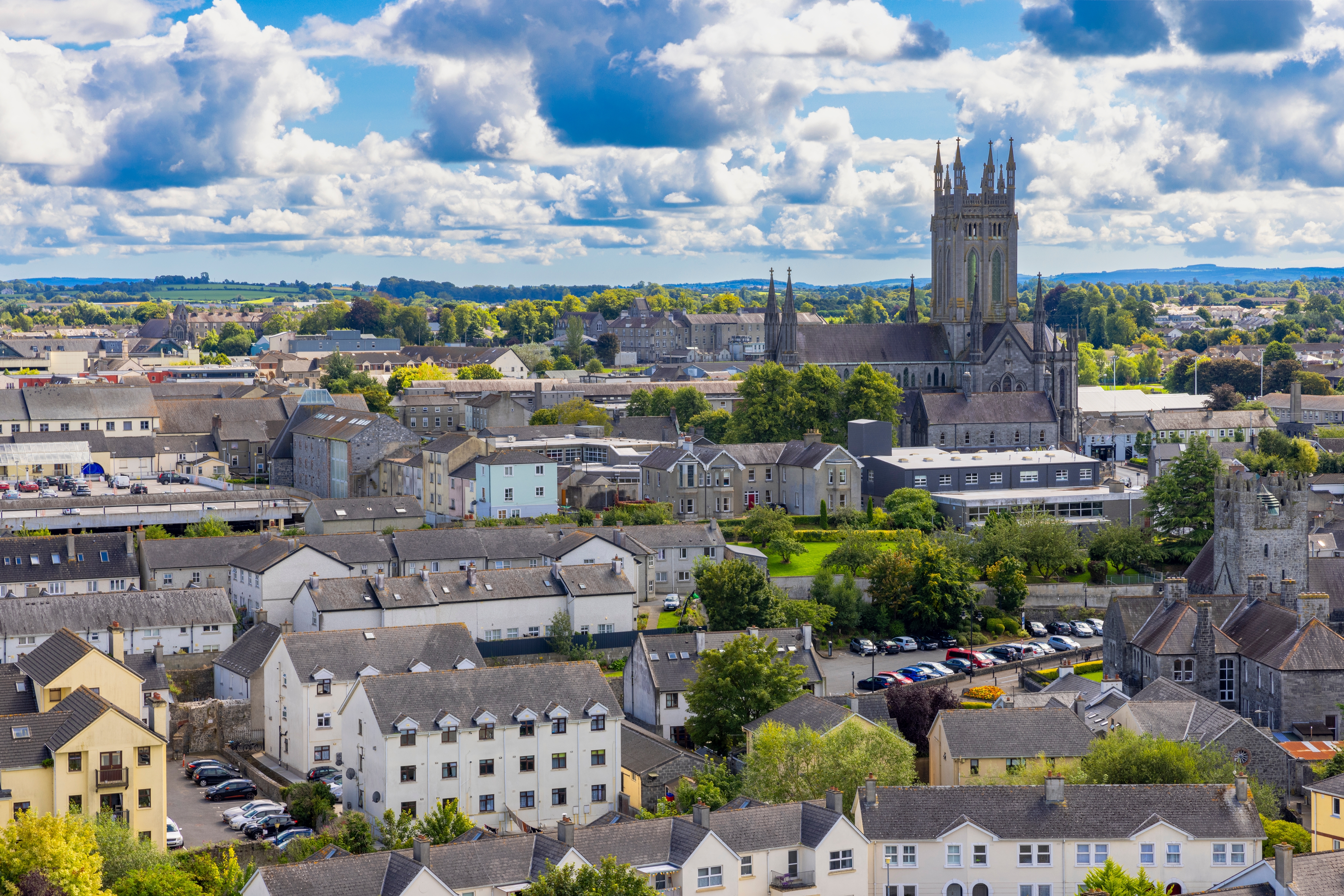 Luftfoto af den historiske by Kilkenny i Irland med den ikoniske katedral, der rejser sig over byens traditionelle bygninger under en blå sommerhimmel