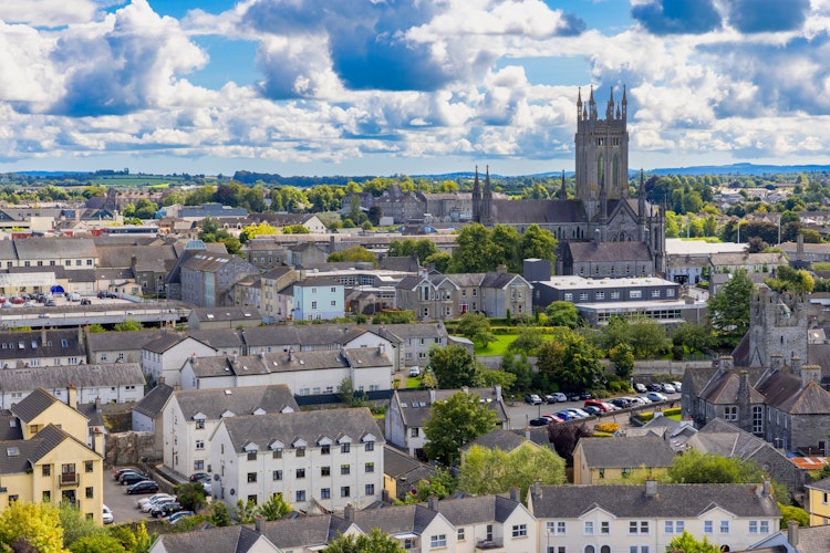 Luftfoto af den historiske by Kilkenny i Irland med den ikoniske katedral, der rejser sig over byens traditionelle bygninger under en blå sommerhimmel
