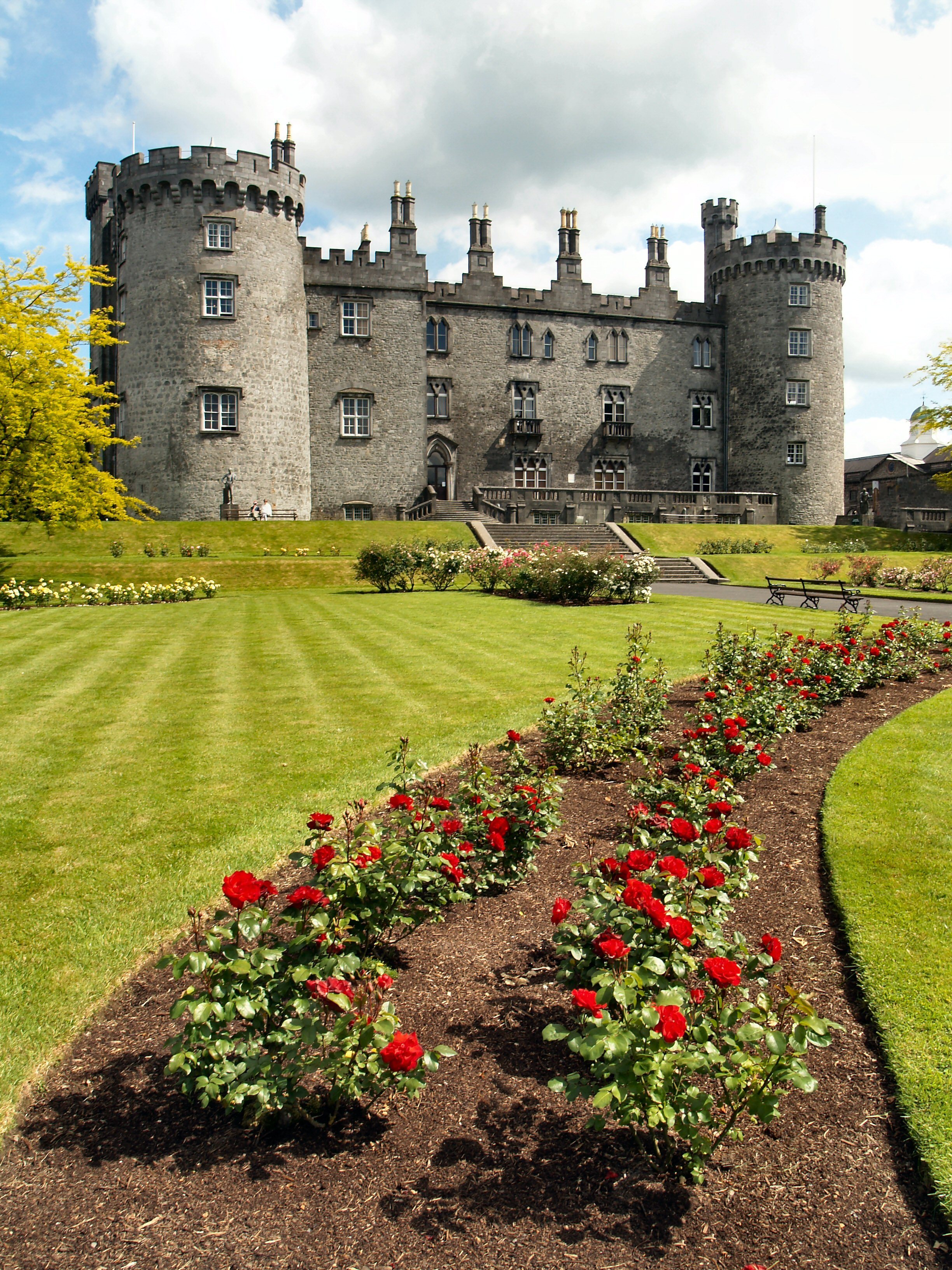 Det historiske Kilkenny Slot i Irland med farverige rosenhaver og velholdte græsplæner under blå himmel