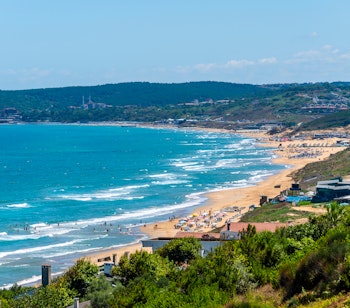 Malerisk udsigt over Kilyos-stranden ved Istanbul om sommeren, med gyldent sand og dramatisk skyet himmel over Sortehavet, hvor farverige strandstole pryder kysten