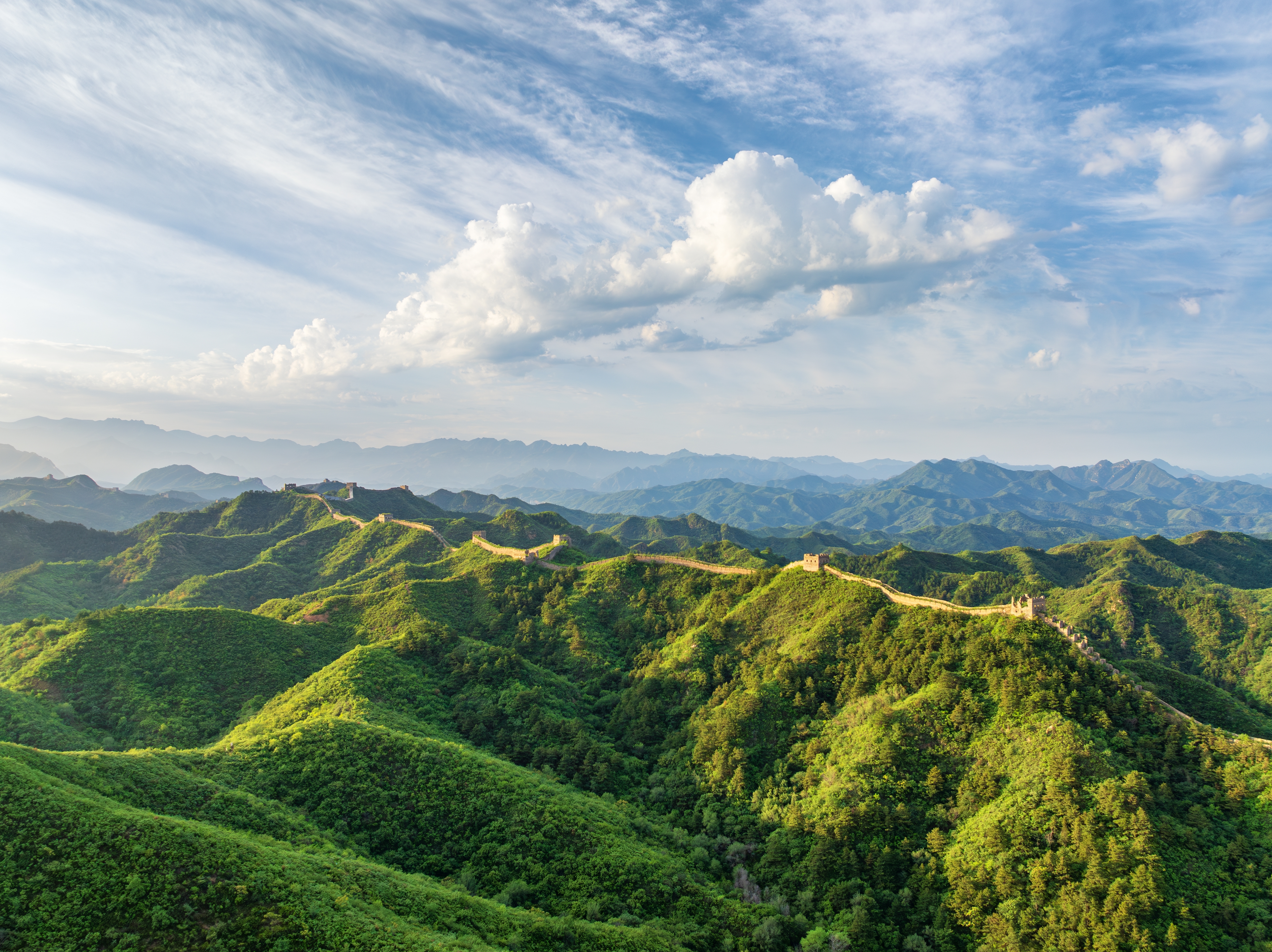 Kinas Store Mur slynger sig gennem grønne bjerge og skovlandskab under blå himmel