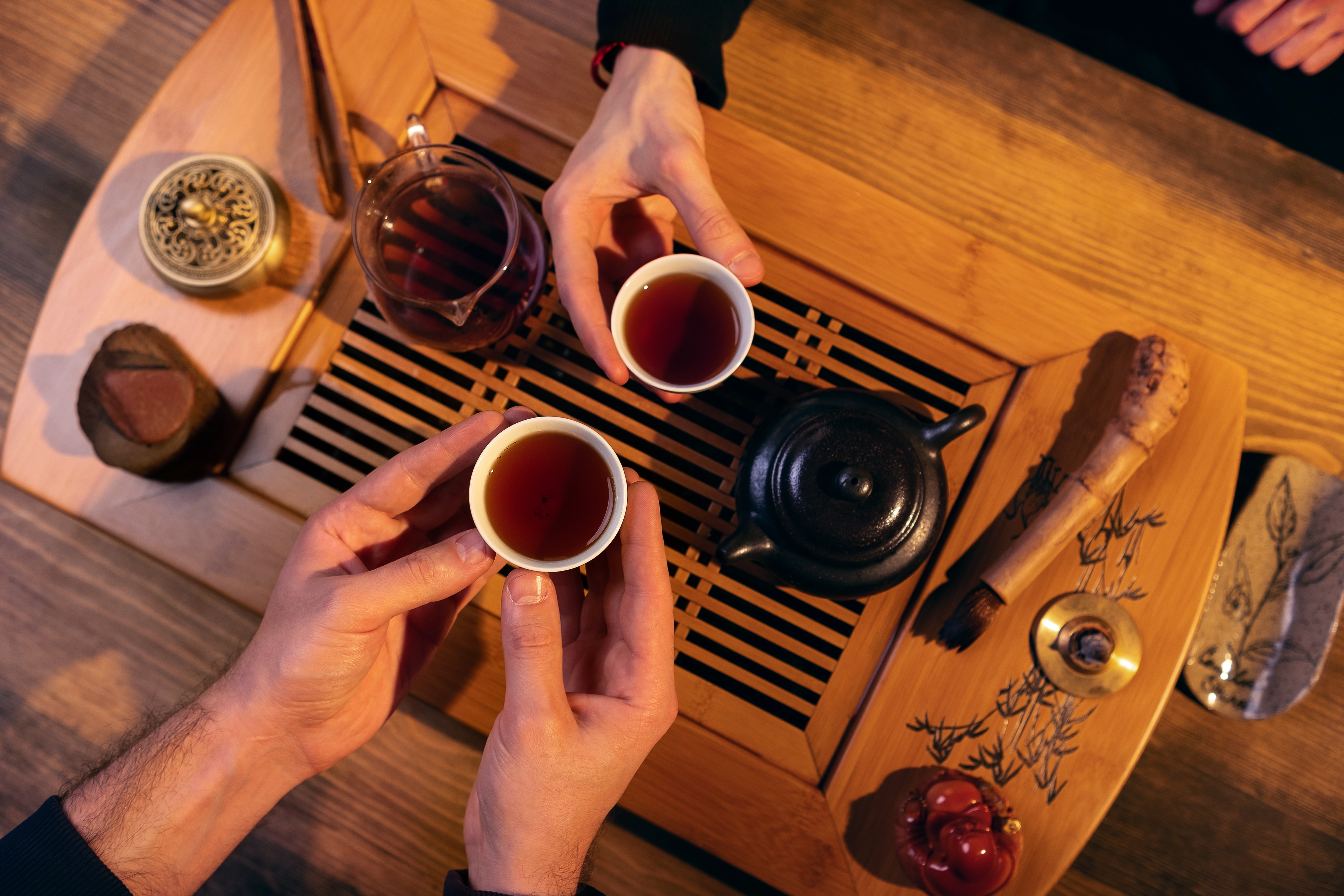 Traditionel kinesisk te-ceremoni med haender der holder tekopper paa traebord under autentisk asiatisk kulturrejse