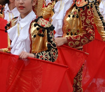 Kinesiske dansere i guldne kostumer udfører traditionel dans med røde silkesjaeler ved kulturfestival