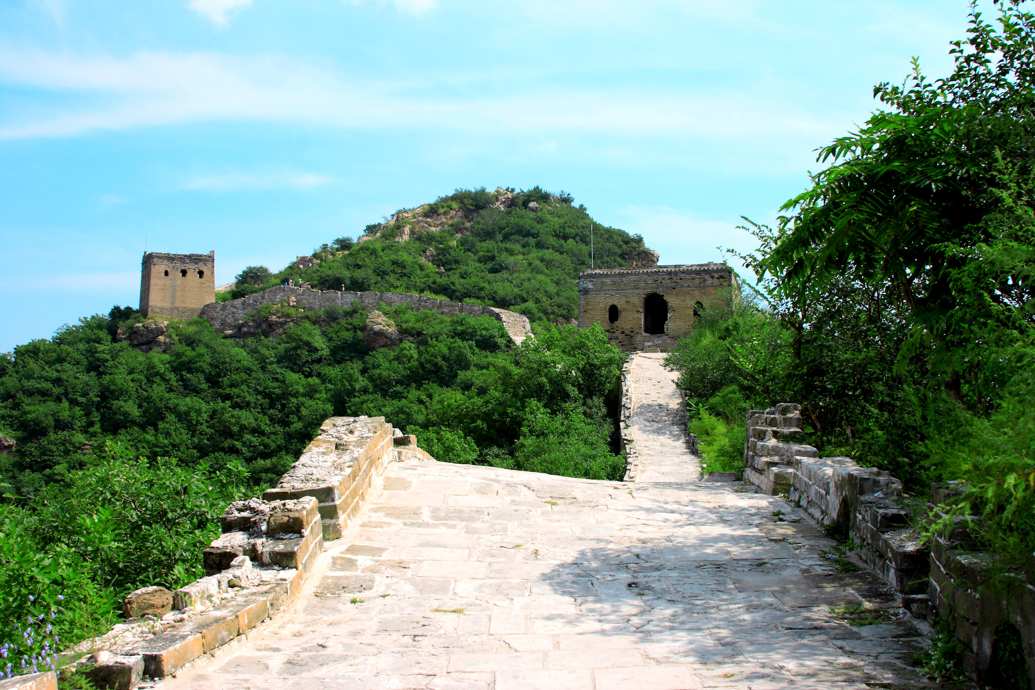 Den Kinesiske Mur slynger sig gennem groenne bjerge under blaa himmel
