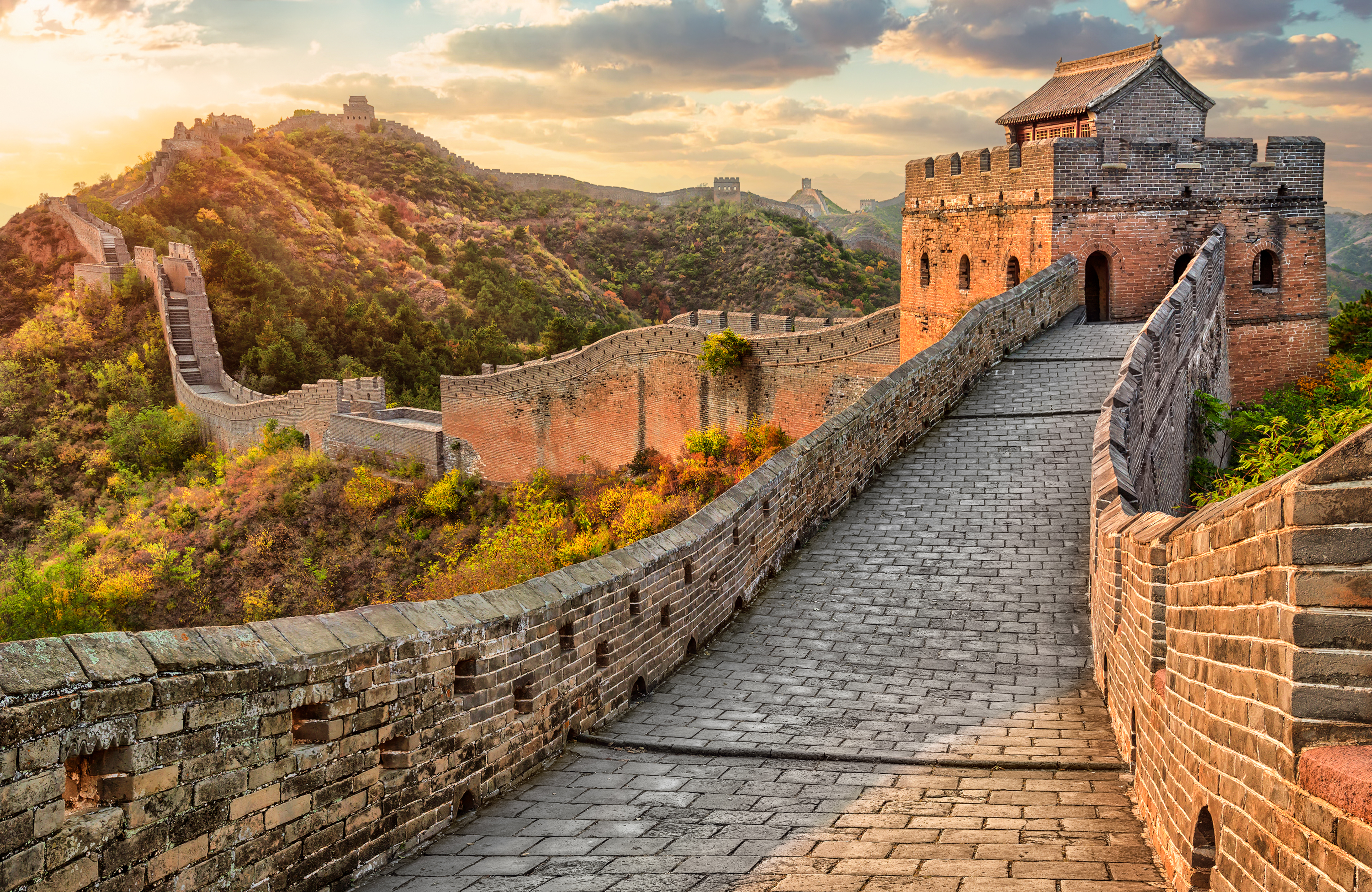 Panoramaudsigt over Den Kinesiske Mur der slynger sig gennem grønne bjerge ved solnedgang