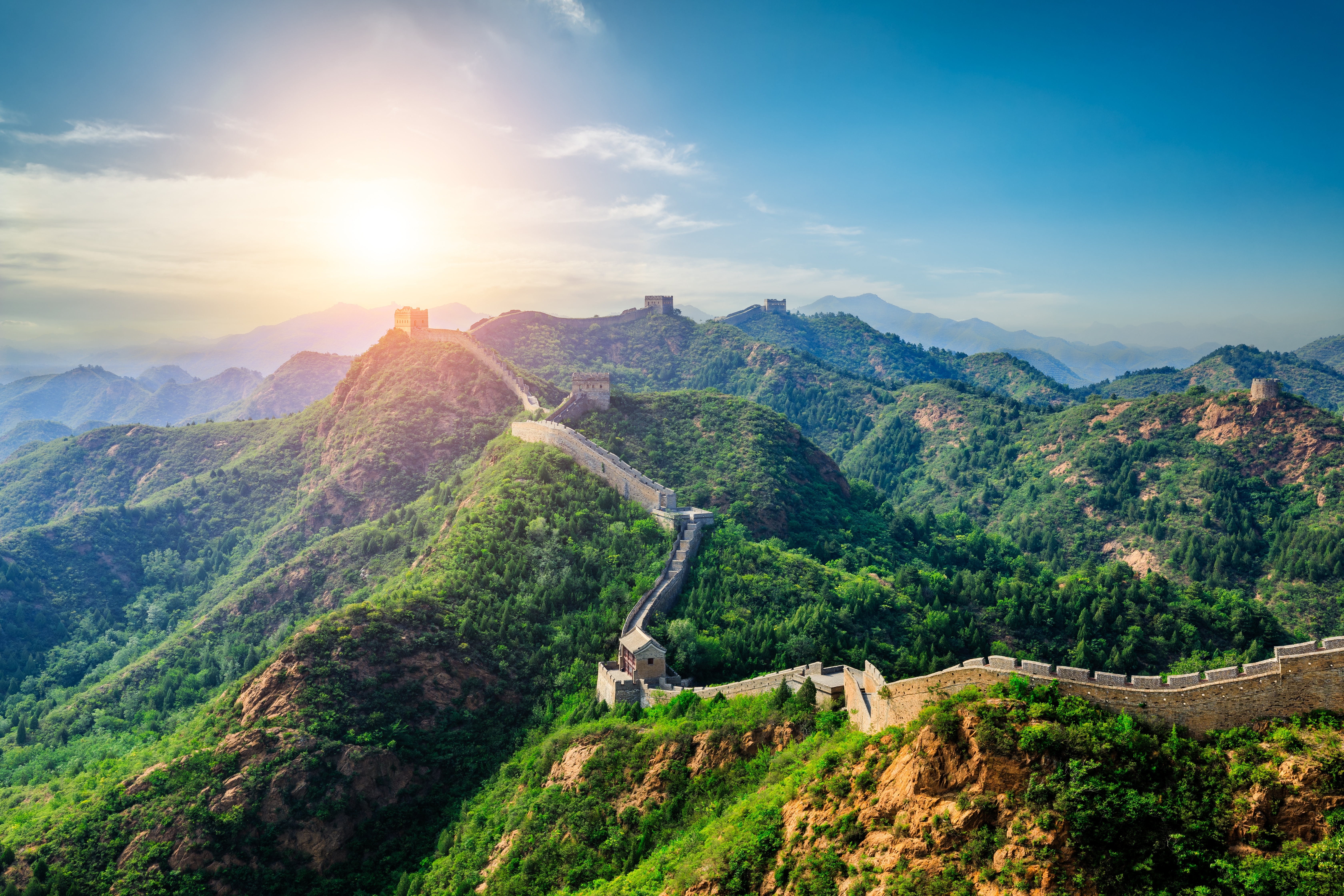 Den Kinesiske Mur slynger sig gennem grønne bjerge ved solnedgang nær Beijing