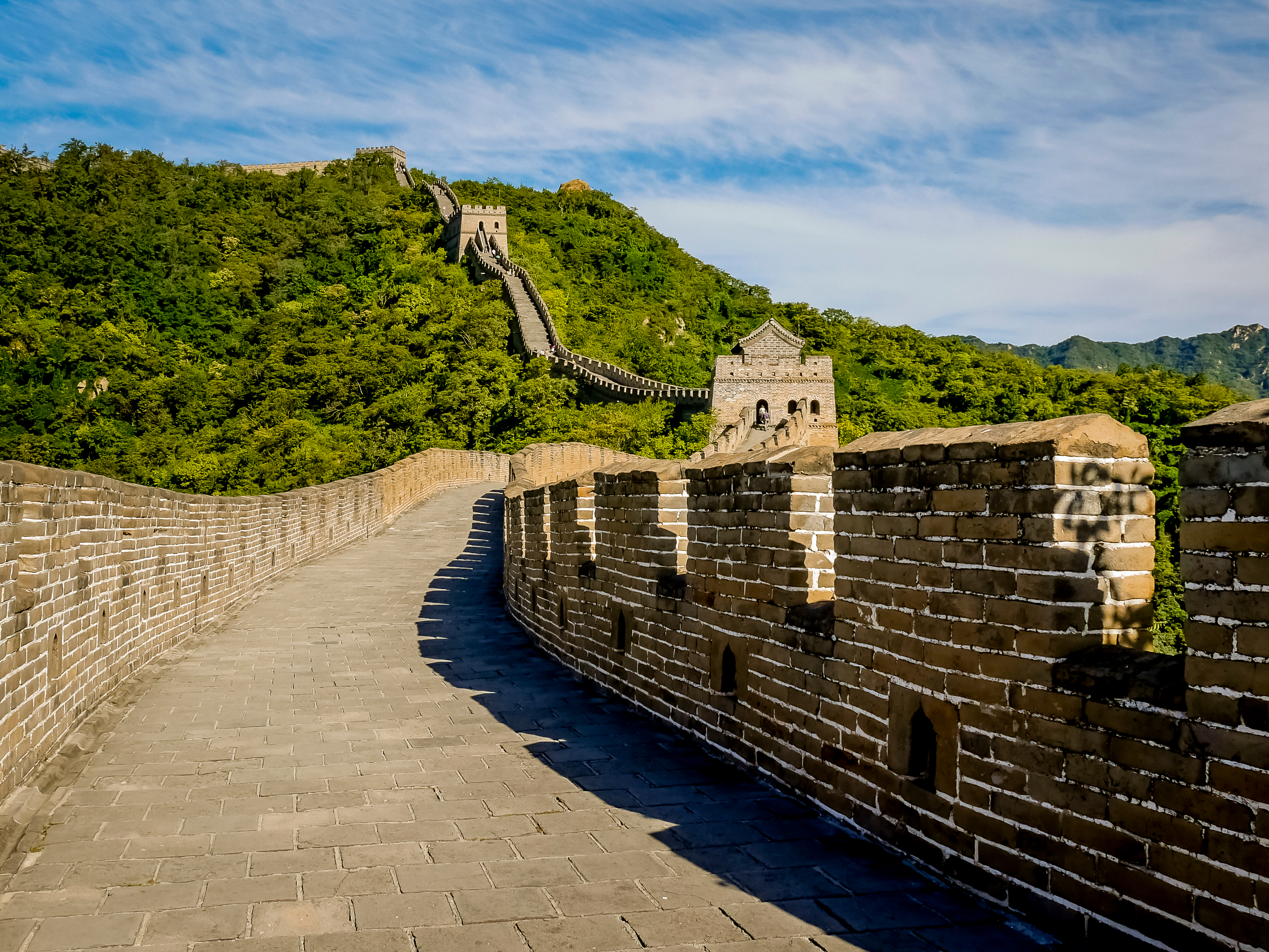 Den Kinesiske Mur slynger sig gennem grønne bjerge med vagttårne og stenbro under blå himmel