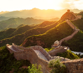 Den Kinesiske Mur slynger sig gennem grønne bjerge ved gyldent solnedgangslys i Kina