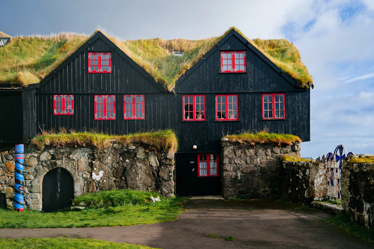 Det historiske Kirkjuboargardur museum i Kirkjubour på Færøerne med traditionelt torvtag og sorte trævægge med røde vinduesrammer