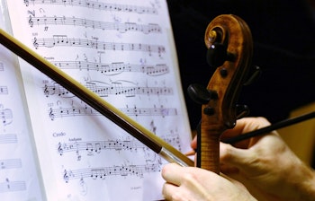 Violinists hånd med bue og blyant over Puccinis Gloria partitur, symboliserer kulturelle musikoplevelser på rejser med Smil Rejser