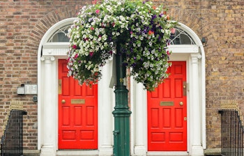To symmetriske røde døre på historiske bygninger i Dublin med karakteristisk irsk arkitektur og blomsterdekorationer