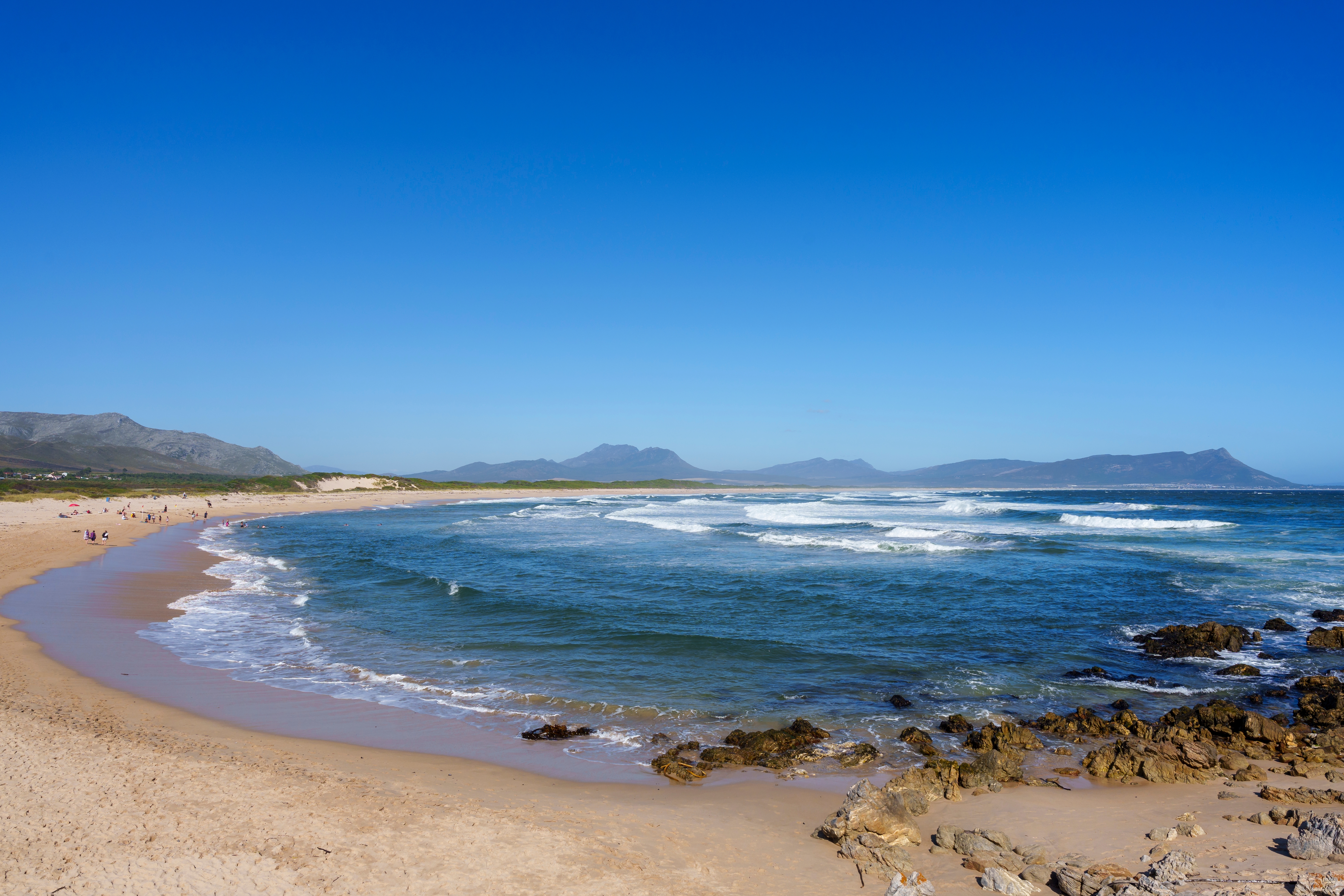 Den smukke Blue Flag-strand ved Kleinmond med turkisblåt hav, bølger og bjerglandskab i Western Cape, Sydafrika