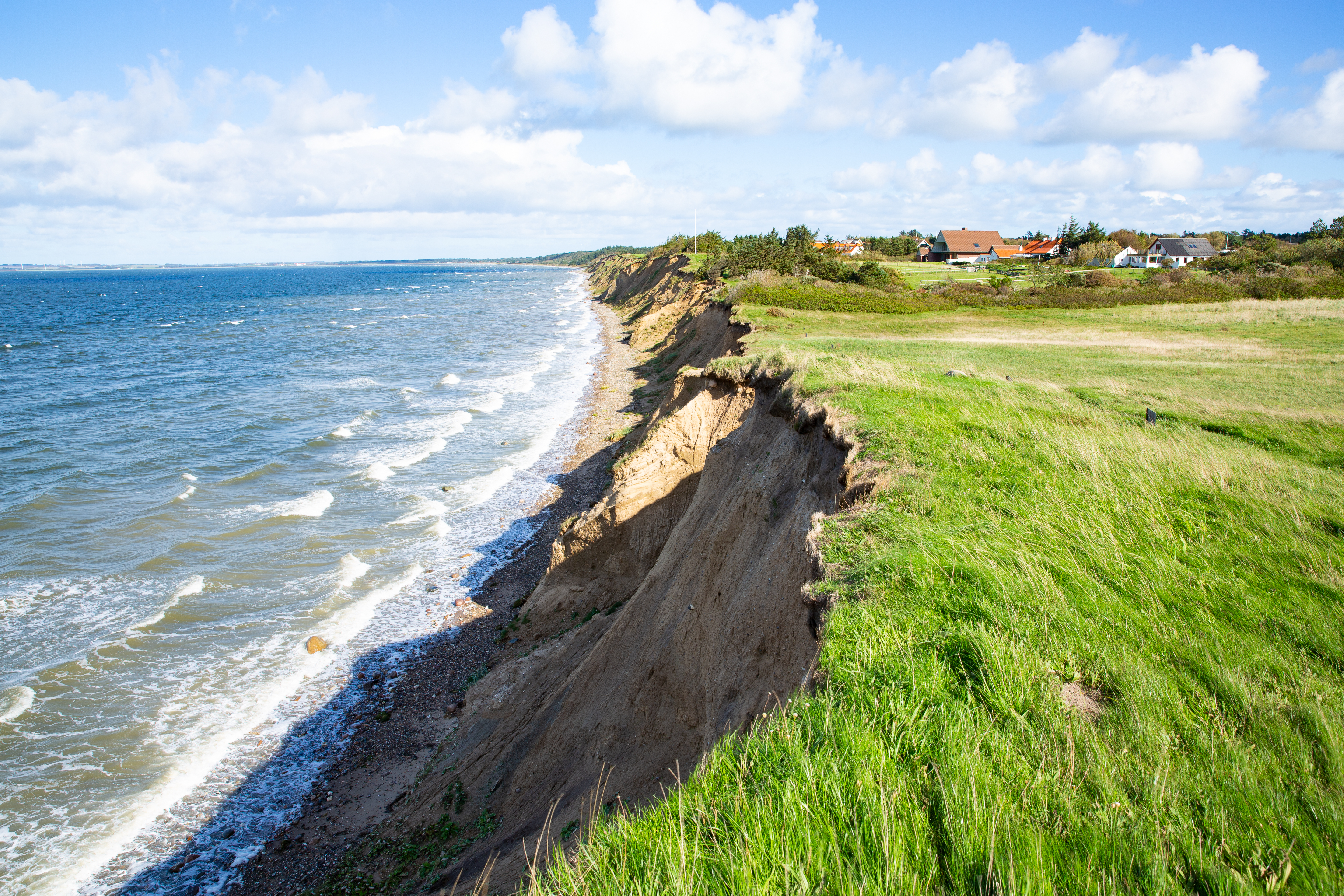 Kliterosion langs Vestjyllands kyst med huse på klippetoppen og grønne marker ved Nordsøen