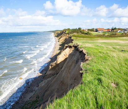 Kliterosion langs Vestjyllands kyst med huse på klippetoppen og grønne marker ved Nordsøen