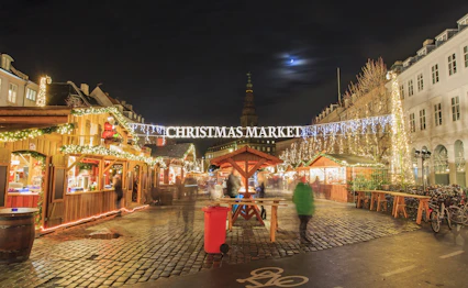 Julemarked i København om natten med festlige lys og træboder under måneskin