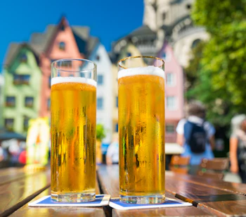 Traditionel Kölsch øl i glas med udsigt til Kølns domkirke og byens skyline i baggrunden