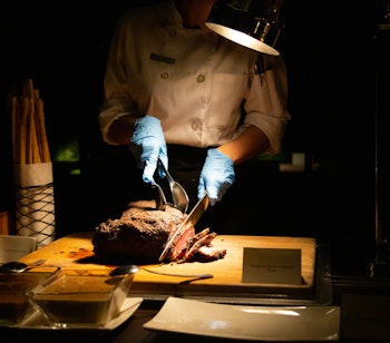 En kok, der omhyggeligt skærer krydret bryst, der viser kulinarisk dygtighed i kødforberedelse.