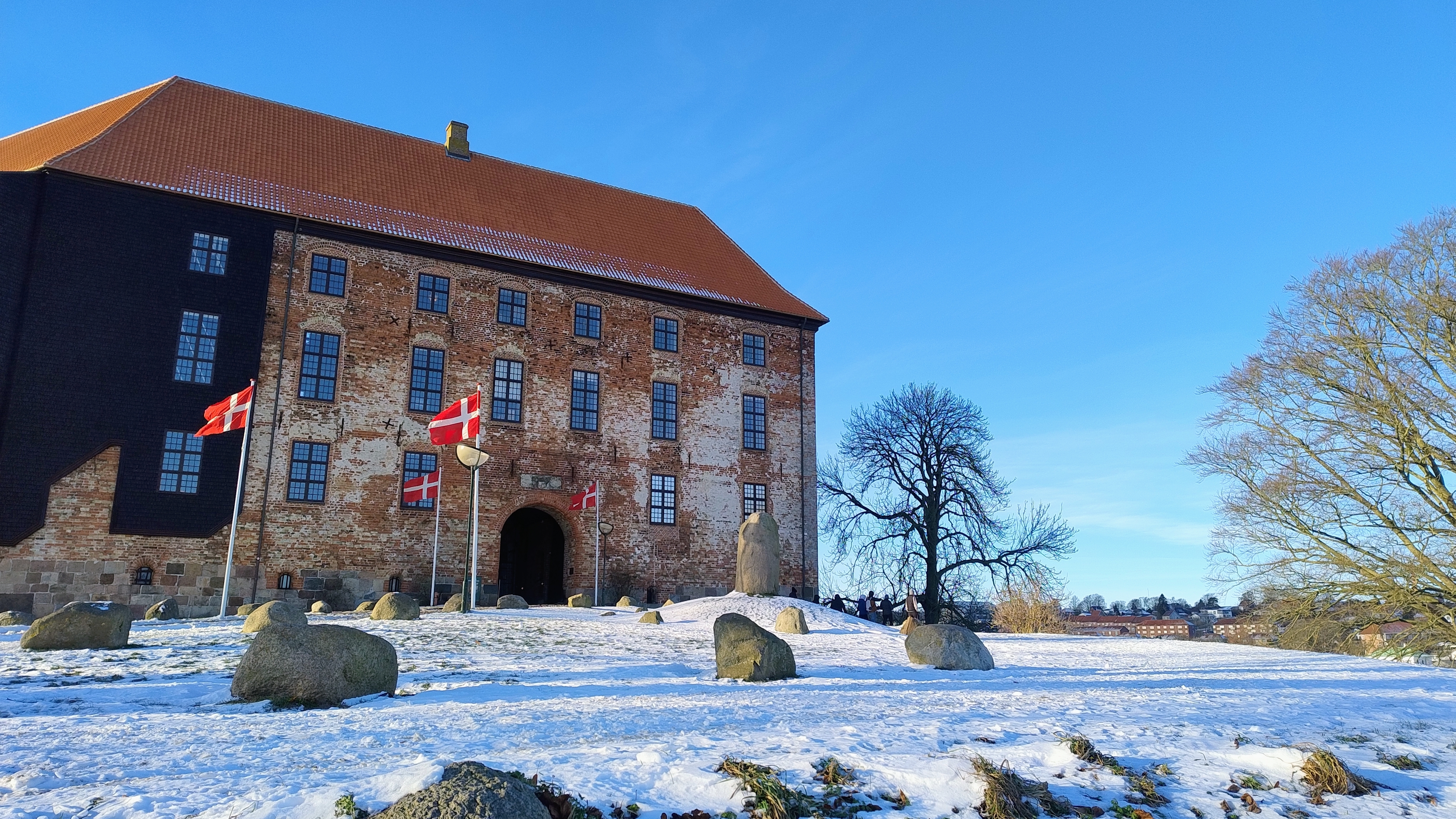 Koldinghus slot i Kolding om vinteren med let sne på jorden, danske flag ved indgangen og blå himmel over den historiske røde tagbygning