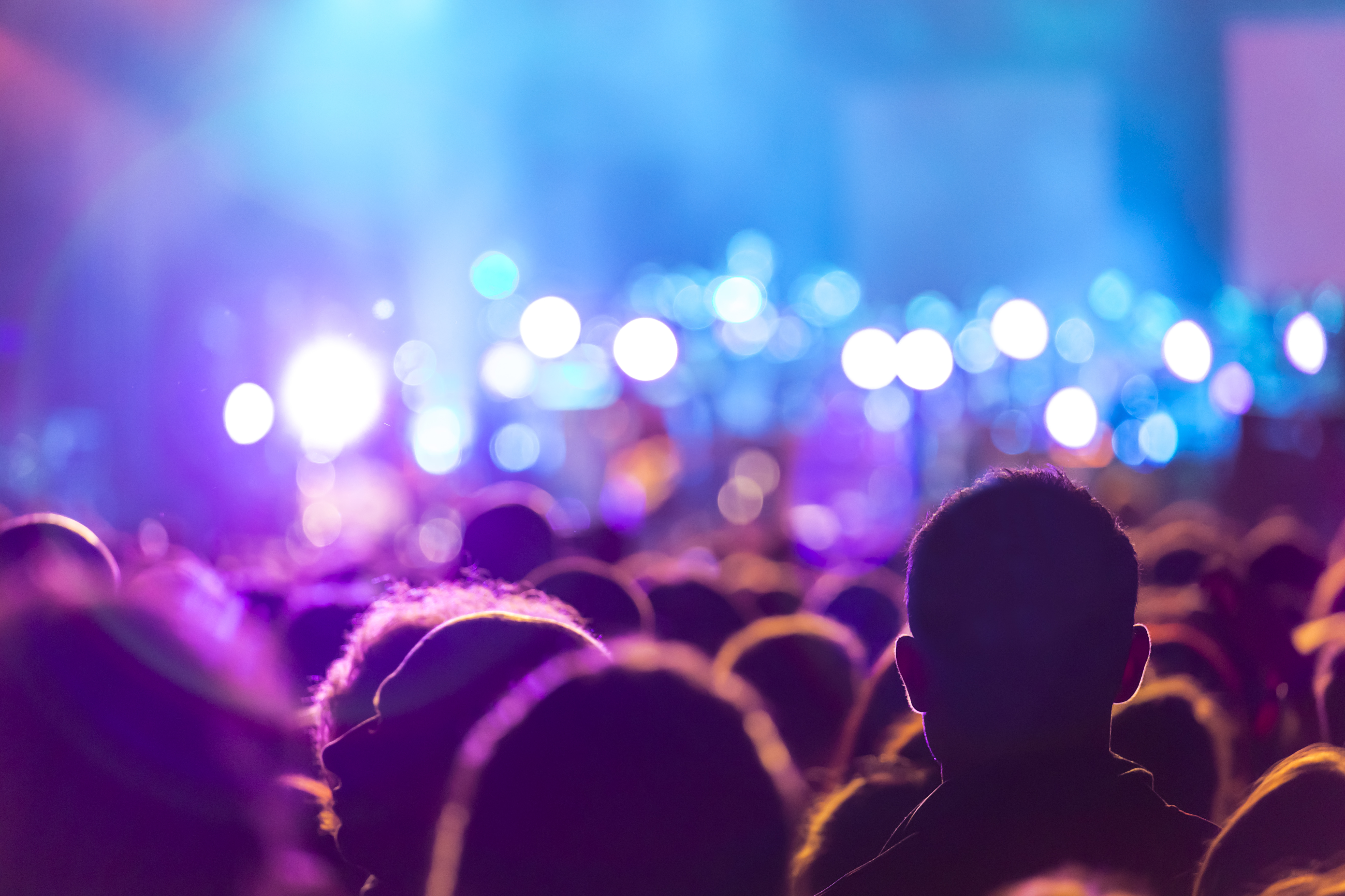 Energisk koncertpublikum med løftede hænder silhuetteret mod blåt scenebelysning, der indfanger den intense stemning og fællesskabsfølelse ved livekoncerter og musikfestivaler