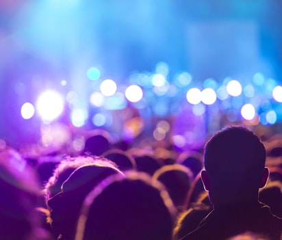 Energisk koncertpublikum med løftede hænder silhuetteret mod blåt scenebelysning, der indfanger den intense stemning og fællesskabsfølelse ved livekoncerter og musikfestivaler