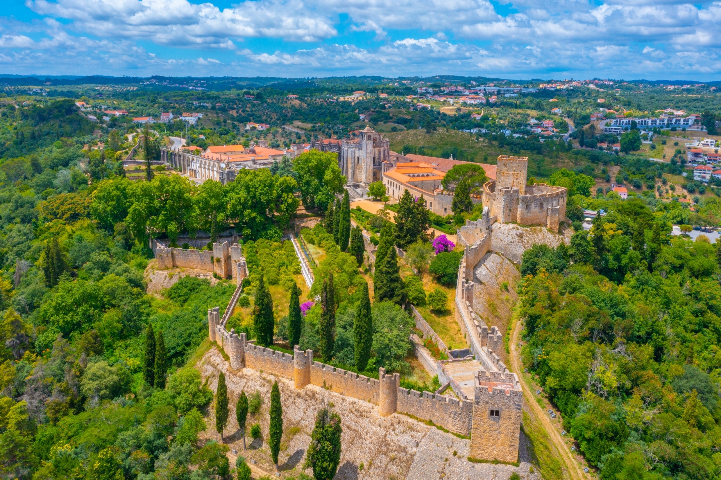 Luftfoto af Kristus-klosteret i Tomar, Portugal - et UNESCO-verdensarvssted omgivet af middelalderlige borgemure og grønne træer