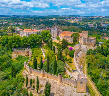 Luftfoto af Kristus-klosteret i Tomar, Portugal - et UNESCO-verdensarvssted omgivet af middelalderlige borgemure og grønne træer